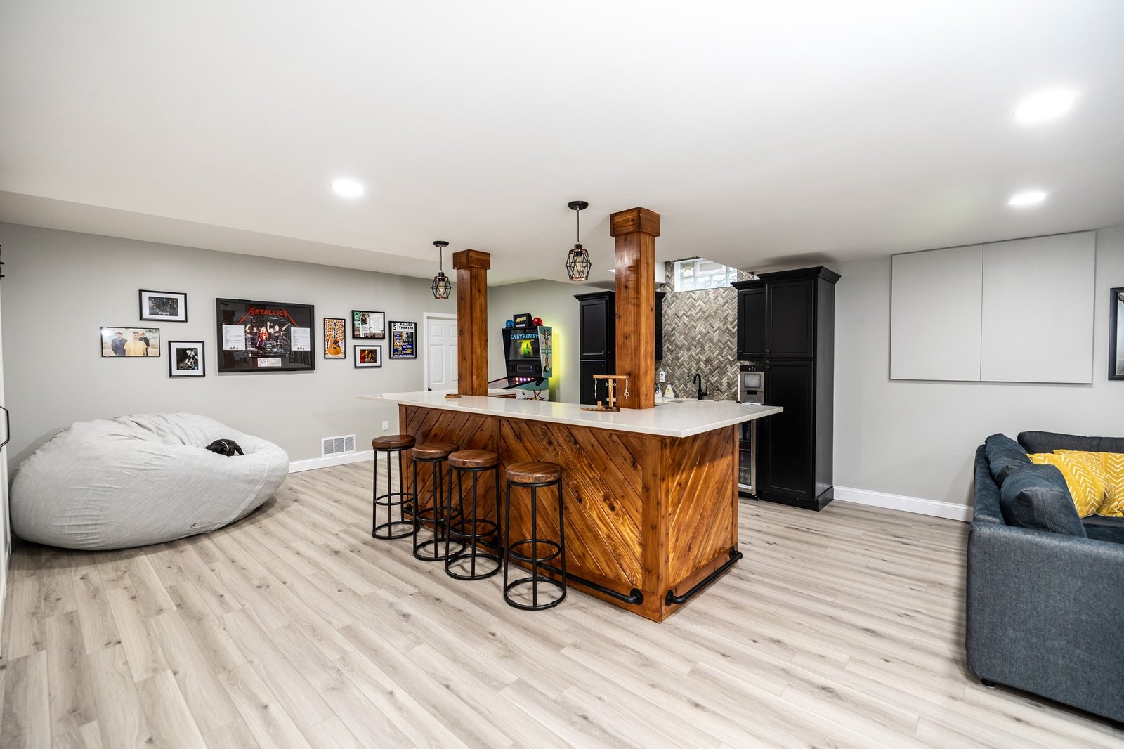 Finished basement with a chevron-clad cedar bar, lounge seating and a pinball machine