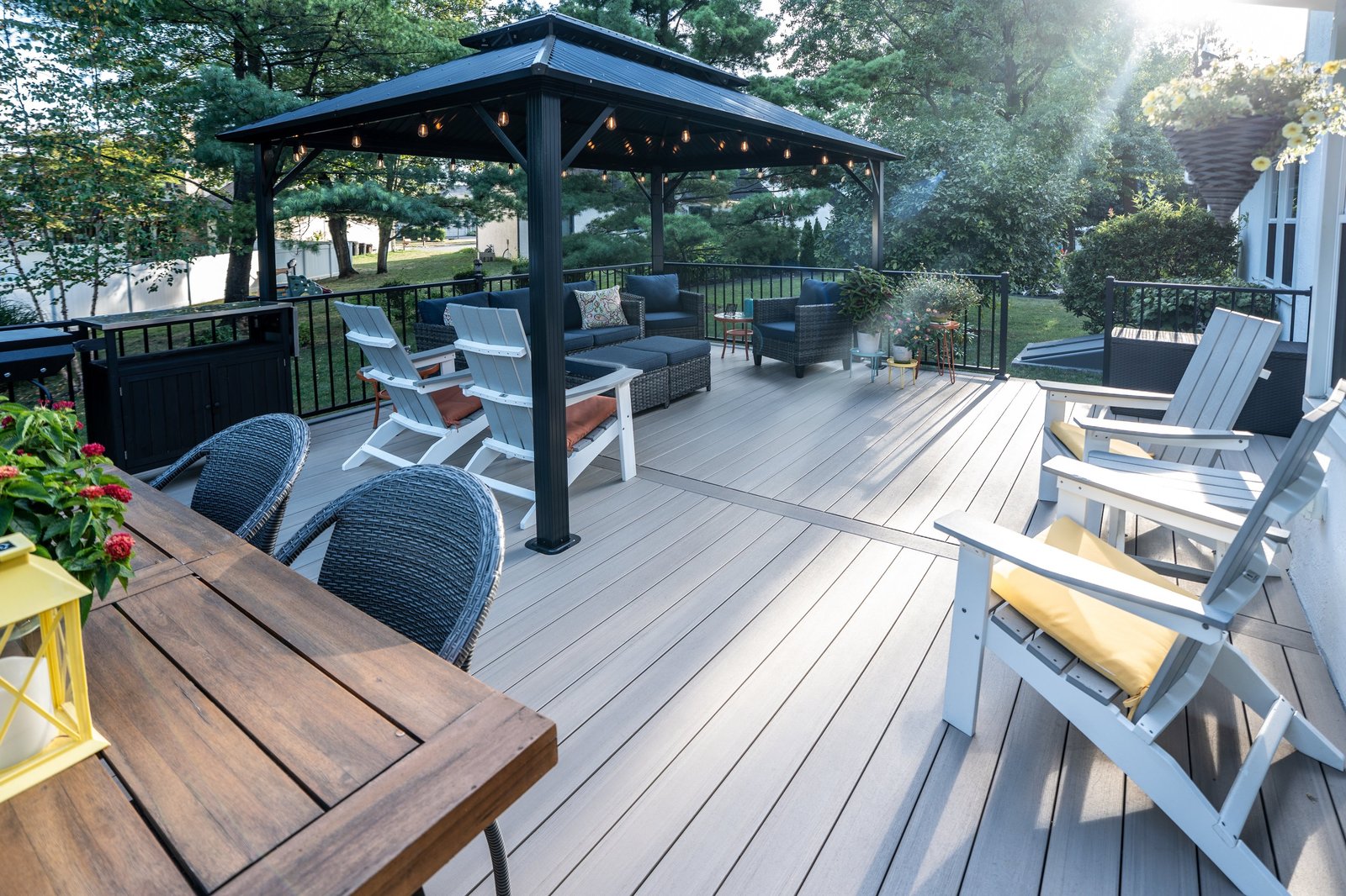 Composite deck with a black metal gazebo, string lights and Adirondack chairs at sunset